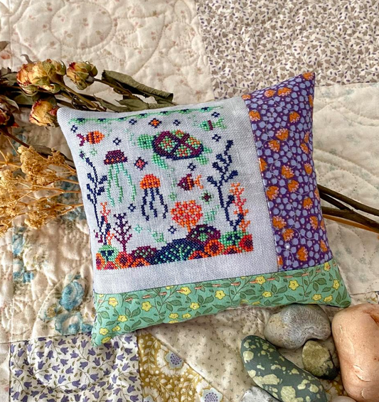 Cross-stitched pillow with underwater scene design on a textured fabric background