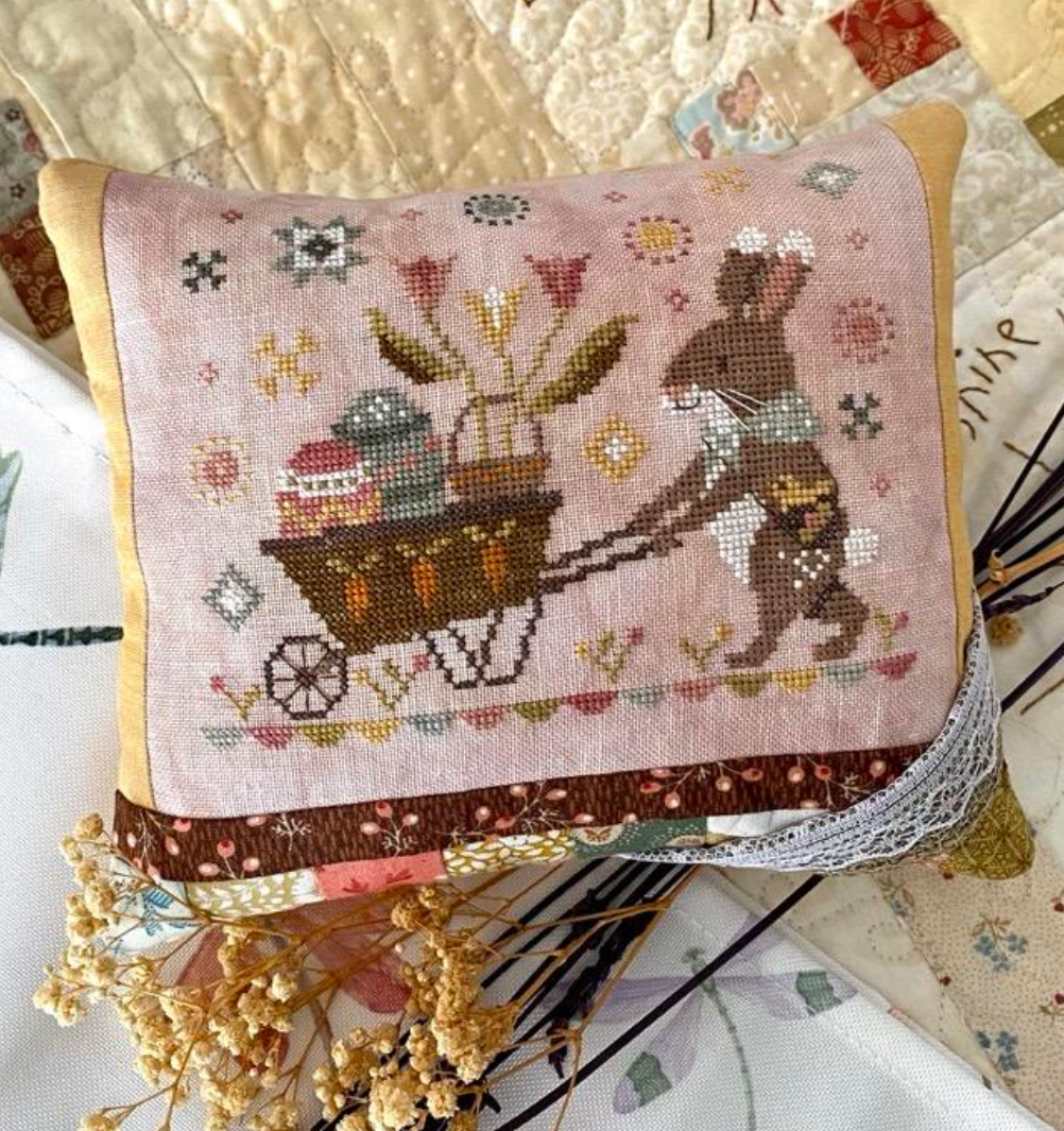 Embroidered pillow with a bunny delivering an Easter basket, on a textured surface.