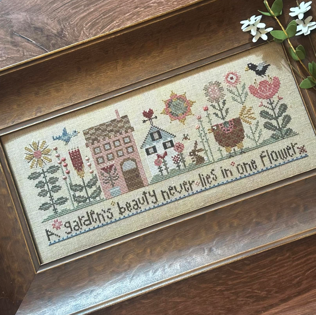 Cross-stitched sampler with floral and architectural design on a wooden frame.